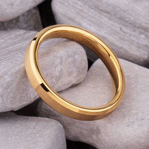 Yellow gold tungsten wedding ring on natural stones, featuring a brushed finish and polished beveled edges.