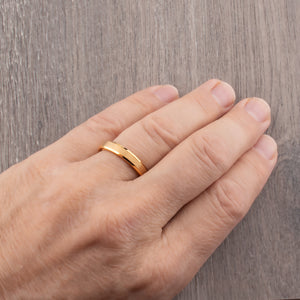 Close-up of a hand wearing a yellow gold tungsten wedding ring showcasing a brushed finish and polished beveled edges.